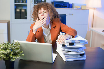 Tired young woman working late at the office, looking sleepy, using smartphone, wanting to relax,...