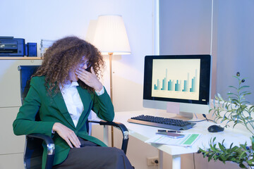 Tired young woman working late at the office, looking sleepy, using smartphone, wanting to relax,...