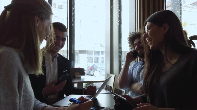 Diverse young professionals collaborate and discuss innovative business ideas at a modern cafe, utilizing laptops and smartphones for a productive meeting in a relaxed urban setting, - Powered by Adobe