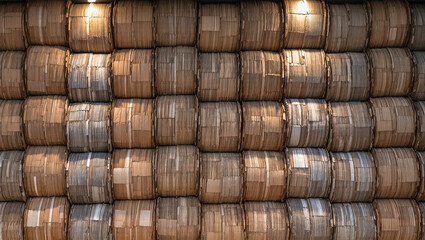A close-up, panoramic shot of a wall made of stacked, compacted bales of recycled paper or cardboard. The uniform, rustic texture of the bales creates a natural and organized pattern.