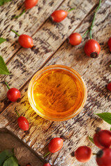 Red rosehip seed oil in a bowl with fresh rose hips