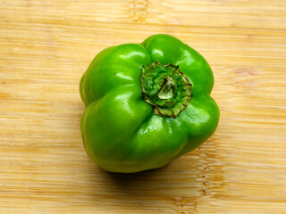 A top down photograph of a fresh and bumpy green bell pepper with its stem cut short placed on a wooden cutting board ready for healthy food preparation