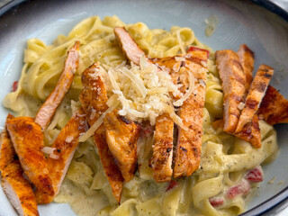 Close-up of pasta with grilled chicken and parmesan in creamy sauce. Gourmet cuisine, indulgence, and food lifestyle in restaurant dining culture.