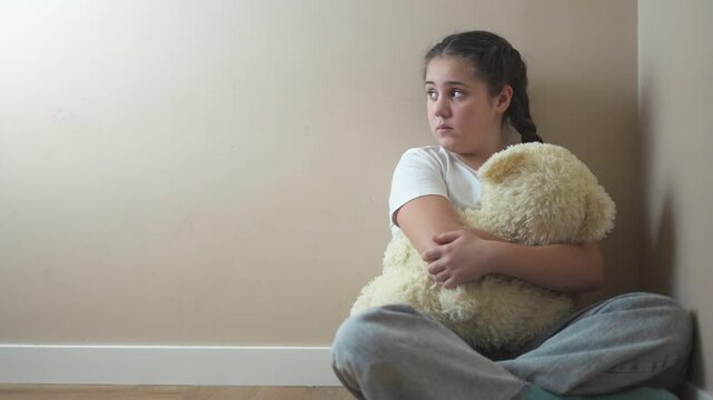 Young girl sitting on the floor with teddy bear. Teddy bear punished by sad corner. Teenage girl is traumatized by a violent attack by a teenager. A young girl is lifestyle seated on the floor with a.