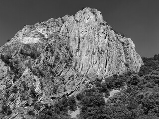 Rocky Cliff Face – Sunlit Mountain Wall Against Clear Sky, Monochrome Hues.