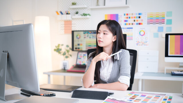 Thoughtful young designer holds pen while analyzing designs on a large screen.