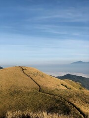 Scenic mountain landscape with a winding hiking trail leading to the summit through vast golden fields of grass