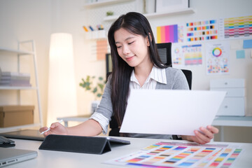 Young graphic designer uses a digital pen and tablet while reviewing color swatches.