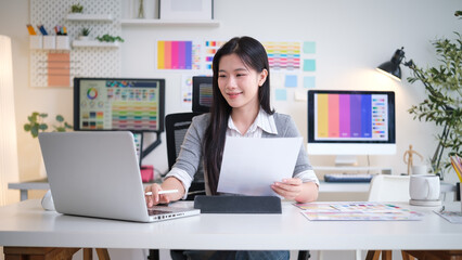 Female designer analyzing color palettes while working on her laptop in a creative office.
