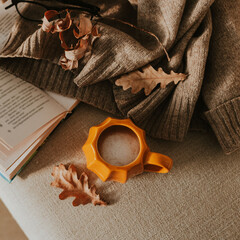 Cozy Autumn Setting with Pumpkin Mug with Coffee, Open Book, Cozy Warm Sweater and Seasonal...