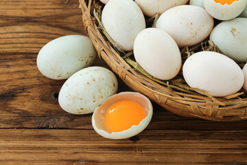 Fresh Duck Eggs in Wicker Basket on Wooden Background with Cracked Egg Showing Orange Yolk
