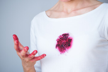 A hand grips ripe blackberries, their juice staining fingertips and a white shirt nearby. The...