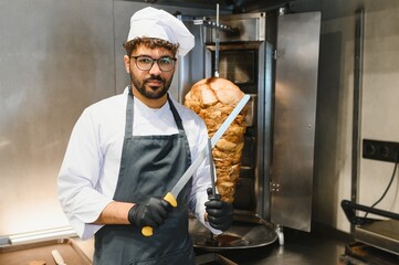 Cook holding knives and preparing shawarma in a restaurant kitchen