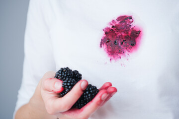 A hand grips ripe blackberries, their juice staining fingertips and a white shirt nearby. The...