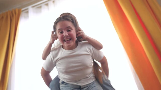 Young boy and little girl sitting on bed. Brother and sister play back roll. Child pulls out pair of ears from a play room. A young boy and a lifestyle small girl are seated on a bed.