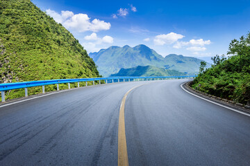 Winding asphalt highway curves through a majestic mountain landscape with green hills under blue sky