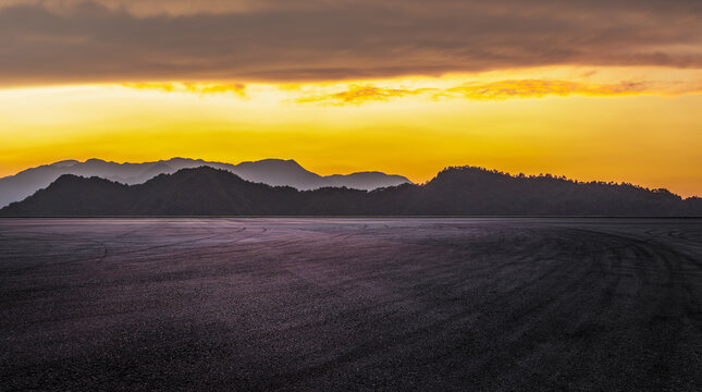 Empty asphalt race track with tire marks and beautiful mountain silhouette under a dramatic golden sunset sky - Powered by Adobe