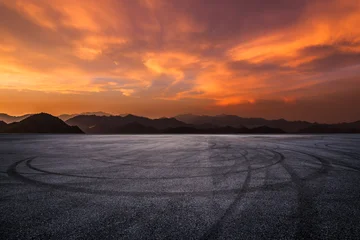 Fototapete Rund Tiefes Orange Empty asphalt race track with tire marks and beautiful mountain silhouette under a dramatic sunset sky  © ABCDstock