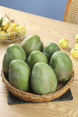 Fresh Green Mangoes in Wicker Basket on Wood Table with Tropical Fruits Kitchen Display