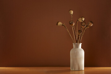 Various dried poppies in a vase on wooden background. Contains copy space.