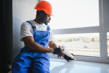 Workman in overalls installing or adjusting plastic windows in the living room at home