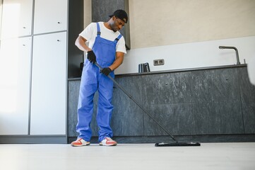Man janitor with mop in hands from cleaning service washing gray floor in uniform.