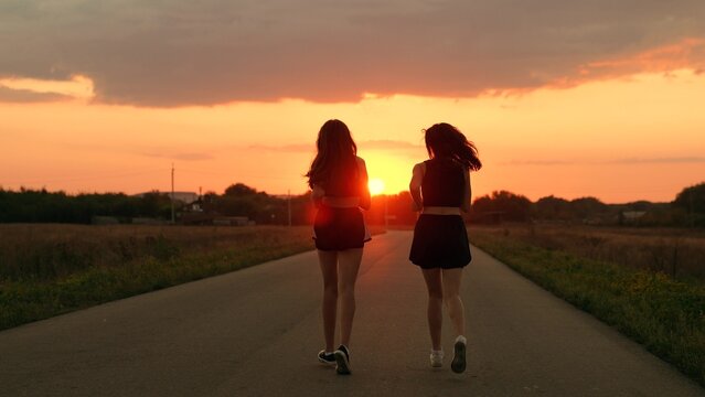 Girls are training, running along road, teamwork of athletes. Slow motion. Athletic young women running along an asphalt road at sunset, teamwork, healthy fitness lifestyle. People run in sun together