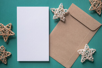 White blank greeting or invitation card and envelope with Christmas decoration on green background.
