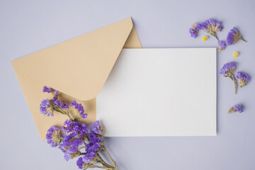 White blank greeting or invitation card with envelope and purple flower decoration on light grey background.
