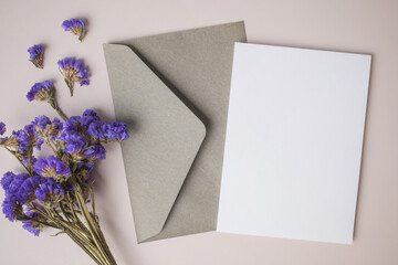 White blank greeting or invitation card with envelope and purple flower decoration on beige...