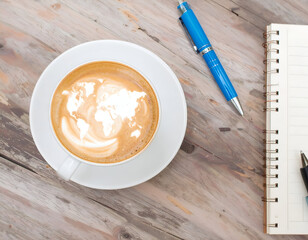 World Map Latte Art in White Cup on Wooden Desk with Notebook and Pen
