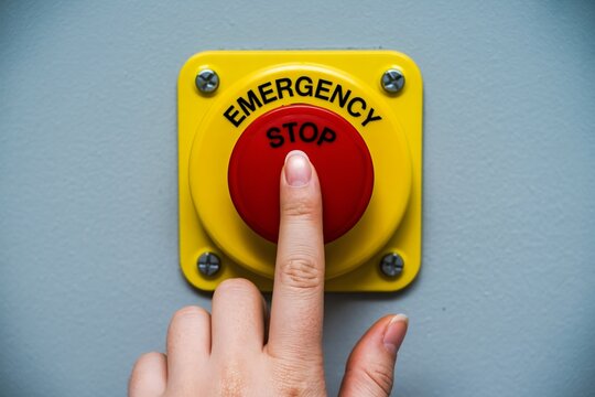 Hand pressing bright red emergency stop button for safety