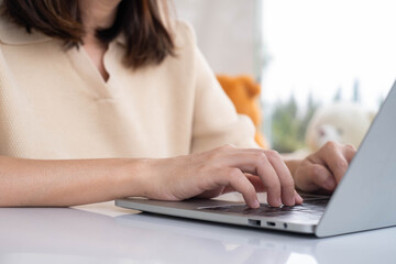Fototapeta premium Close-up of Asian woman typing on laptop keyboard at home. Concept of remote work, freelancing, online communication, digital workspace, technology usage, or productivity in modern lifestyle.