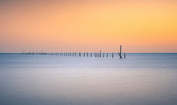 Serene sunset over calm ocean with wooden posts.