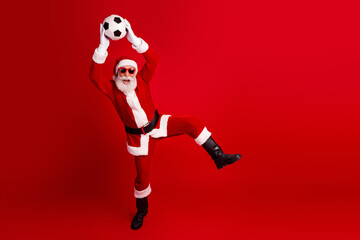 Santa Claus wearing sunglass playing soccer holding a ball against a red background for Christmas fun and joy