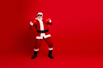 Festive Santa Claus cheerfully posing in a boxing stance wearing sunglass on a vibrant red background, celebrating Christmas