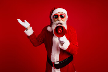 Santa Claus in sunglass holding a megaphone on a red background, spreading holiday spirit and...