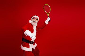 Elderly Santa Claus Playing Tennis in Fun Costumed Scene with Red Background and Holiday Cheerful Spirit