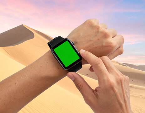 Close-up of a person's hand adjusting a smartwatch with a green screen in the desert