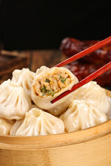 Chinese Soup Dumplings Xiao Long Bao with Meat Filling in Bamboo Steamer Held by Chopsticks