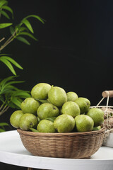 Fresh Green Walnuts in Wicker Basket on White Table with Tropical Plants Background