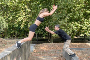 Two athletes practicing parkour, jumping over concrete walls in a park, performing stunts and demonstrating agility