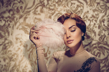 Retro fashion portrait of young pretty lady posing with white feather. Elegant retro woman holding...