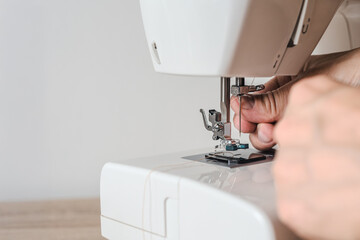 Male tailor threading a needle in sewing machine making handmade clothes. Close-up of male hands inserting thread into sewing machine needle mechanism