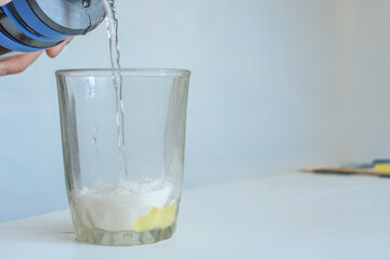 Pouring water in glass with yellow protein banana powder. Pouring water into glass to mix protein powder supplement, preparation stage