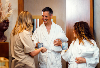 Spa worker offering welcome tea to middle-aged couple entering luxury wellness center.