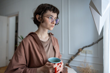 Sad upset teenage girl looks out window disappointedly at home suffers from bullying feeling...