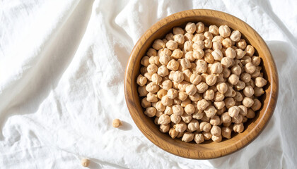 Close-up shot of a wooden bowl filled with dried chickpeas on a white cloth.