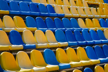 Empty yellow and blue plastic seats in long rows at a sports stadium; bright bleachers pattern for football, baseball or track event backdrops and banners. Photo