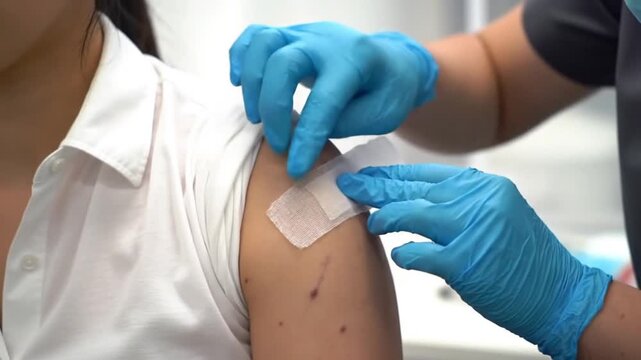 Healthcare Professional Applies Bandage to Patients Arm After Medical Procedure or Vaccination